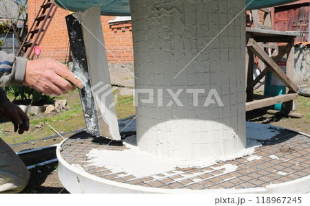 male hand with wide spatula applies layer of mastic on round wide table base, outdoor plastering work on interior and garden furniture male hand with wide spatula applies layer of mastic on round wide table base, outdoor plastering work on interior and garden furniture 118967245