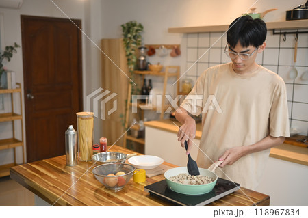 Young man stirring ingredients in a green pan with spatula. People, food and lifestyle concept 118967834