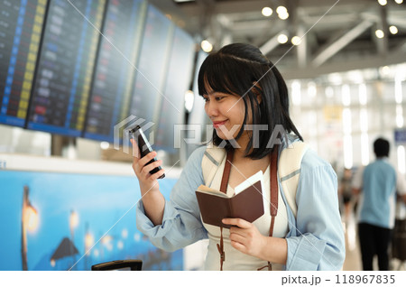 Happy young woman holding her passport and using smartphone at an airport terminal Happy young woman holding her passport and using smartphone at an airport terminal 118967835