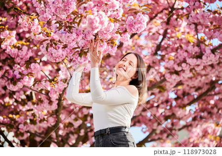 Woman allergic enjoying after treatment from seasonal allergy at spring. Portrait of happy beautiful woman smiling in front of blooming sakura tree at springtime. Spring allergy concept. 118973028