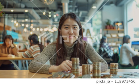 Bright coworking space featuring Asian woman stacking coins, shared table, diverse group, friendly and collaborative atmosphere. Asian woman making stack of coin 118973450