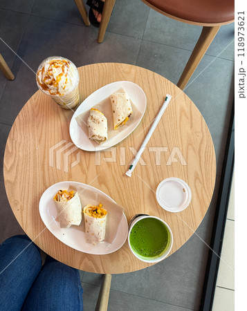Healthy snack and drink on a wooden cafe table. Enjoy a delicious and nutritious break with wraps and vibrant beverages. Healthy snack and drink on a wooden cafe table. Enjoy a delicious and nutritious break with wraps and vibrant beverages. 118973621