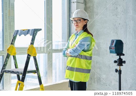 Woman in safety vest hard hat with crossed arms on new residential or commercial real estate site 118974505