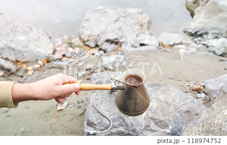 Brewing coffee outdoors with a vintage pot by the riverside on a rocky terrain 118974752