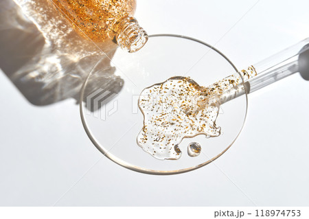 Luxurious gold-infused skincare serum spilled on a glass surface with dropper 118974753