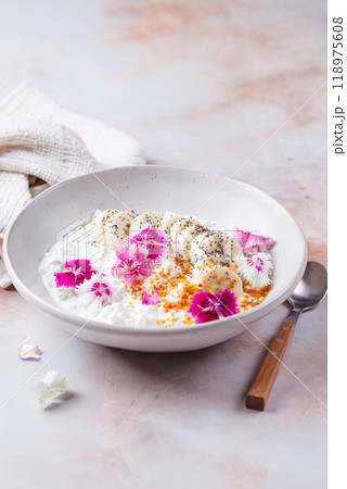 Breakfast cottage cheese with banana and pink culinary flowers, on pink marble background. Breakfast cottage cheese with banana and pink culinary flowers, on pink marble background. 118975608
