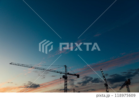 Construction cranes on the background of a sunset sky with clouds Construction cranes on the background of a sunset sky with clouds 118975609