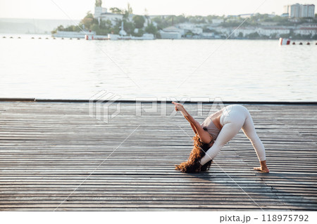 Pretty healthy woman doing active training exercise on a yoga mat near the ocean. Coastal yoga tranquility 118975792
