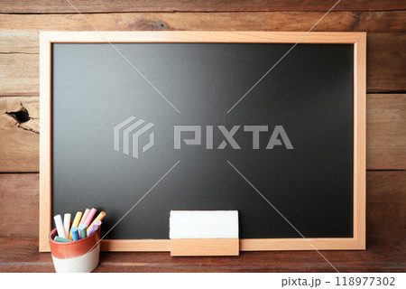 Black chalkboard with colorful chalks and eraser on wooden wall Black chalkboard with colorful chalks and eraser on wooden wall 118977302