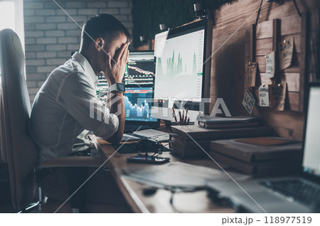 Stressful day at the office. Young businessman holding hands on his face while sitting at the desk in creative office Stressful day at the office. Young businessman holding hands on his face while sitting at the desk in creative office 118977519
