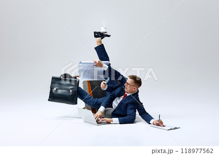 Businessman juggling multiple tasks, papers flying as he multitasks on floor. Overloaded but determined to stay on top of his workload. 118977562