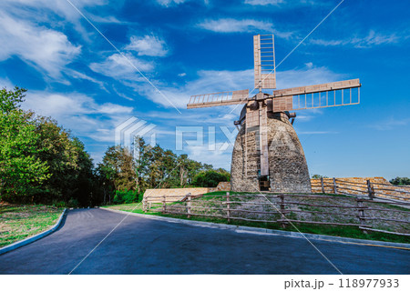Stone windmill stands tall under a vibrant blue sky with scattered clouds. 118977933
