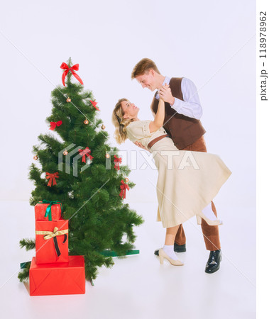 Couple shares romantic moment dancing beside Christmas tree, surrounded by holiday decorations and festive atmosphere. Couple shares romantic moment dancing beside Christmas tree, surrounded by holiday decorations and festive atmosphere. 118978962