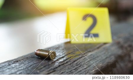 9 mm pistol copper head bullet lying on dark wooden bench with blur number 2 sign on blur background. Concepts of criminal investigations and shooting sport. 9 mm pistol copper head bullet lying on dark wooden bench with blur number 2 sign on blur background. Concepts of criminal investigations and shooting sport. 118980630