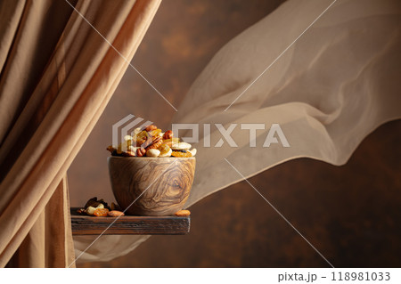 The mix of various nuts and raisins in a wooden bowl on a brown background. 118981033