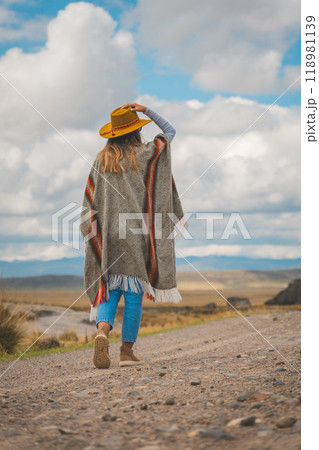 A woman wearing a yellow hat and blue jeans is walking down a dirt road, rock megalithic. Huayllay Stone Forest, Peru. 118981139