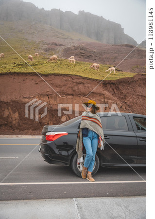 A woman stands in front of a black car, wearing a hat and a scarf, tourist in Huayllay Stone Forest, Peru. A woman stands in front of a black car, wearing a hat and a scarf, tourist in Huayllay Stone Forest, Peru. 118981145