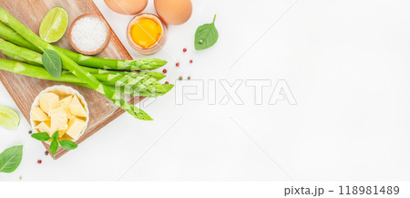 Fresh asparagus on wood board ready for cooking on a white background. cooking concept. Long banner format. top view. copy space for text Fresh asparagus on wood board ready for cooking on a white background. cooking concept. Long banner format. top view. copy space for text 118981489