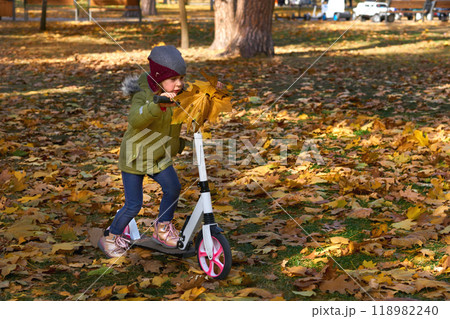 A small child on a push scooter carries a bouquet of autumn leaves to his mother A small child on a push scooter carries a bouquet of autumn leaves to his mother 118982240