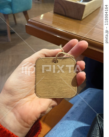 Close-up hand holds a small wooden tag with a twine loop. Copy space and empty place for text. Natural texture and simplicity of the tag create a connection to artisanal craftsmanship 118984164
