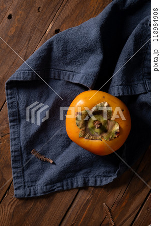 A single ripe persimmon rests on a dark wooden surface A single ripe persimmon rests on a dark wooden surface 118984908