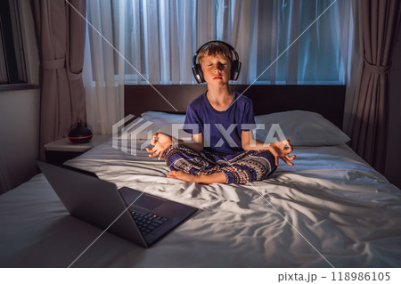 Boy meditates on bed using meditation app. sport, technology and healthy lifestyle concept 118986105