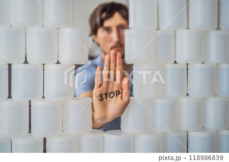 Man showing stop surrounded by many jars of yoghurt that he uses in a year. A huge amount of plastic food jars. Excessive consumption of plastic. Reduce, reuse, recycle 118986839