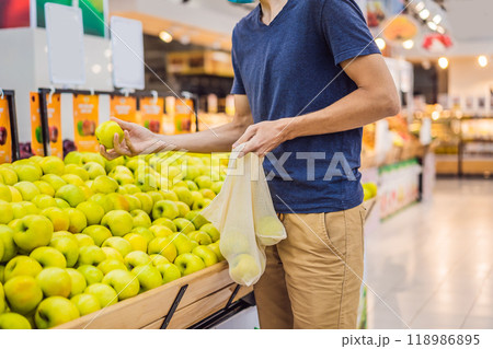Man chooses apples in a supermarket without using a plastic bag. Reusable bag for buying vegetables. Zero waste concept Man chooses apples in a supermarket without using a plastic bag. Reusable bag for buying vegetables. Zero waste concept 118986895