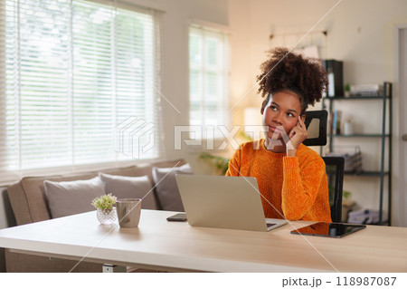 Young black woman in cozy sweater concentrating on laptop at home office during daytime. 118987087