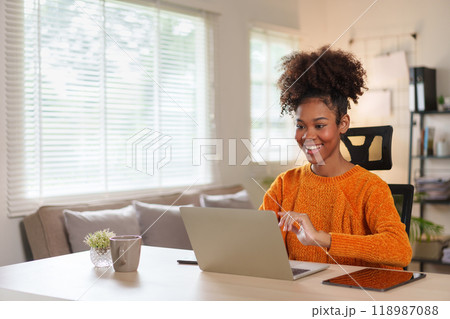 Young African American woman smiling while engaged in virtual meeting at home. 118987088