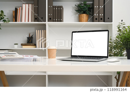 A laptop computer with empty display and office supplies on a desk in front of a bookshelf A laptop computer with empty display and office supplies on a desk in front of a bookshelf 118991164