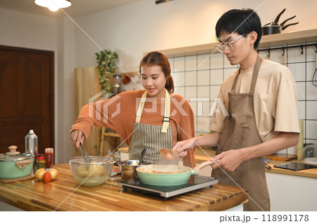 Young couple wearing aprons cooking in a cozy kitchen. Relationships, cooking and happy domestic life 118991178
