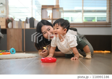 Loving young mother playing with little son on floor at home. Childhood and nurturing care concept. Loving young mother playing with little son on floor at home. Childhood and nurturing care concept. 118991186