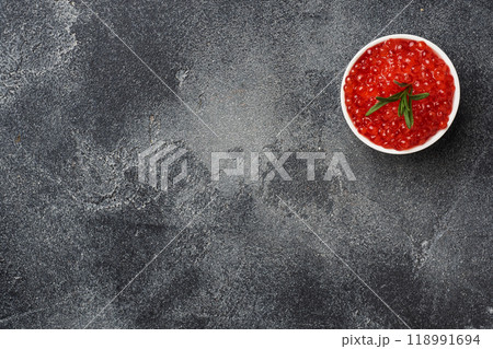 Red salmon caviar in a plate on a dark concrete background. Copy space. Snack delicacy. Red salmon caviar in a plate on a dark concrete background. Copy space. Snack delicacy. 118991694