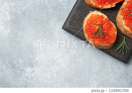 Sandwiches with red caviar on a white baguette with cottage cheese and rosemary. Dark wooden cutting Board. Grey concrete background. Copy space. 118991700