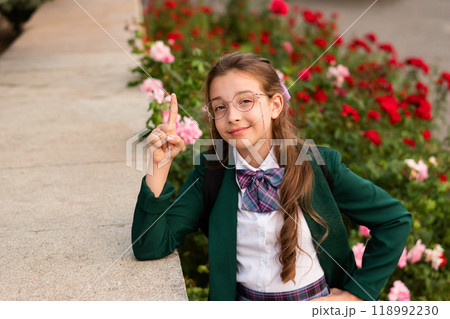 Girl in school uniform smiling and raising finger 118992230