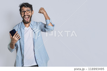 Excited man winning a prize from his cellphone. Excited handsome man looking at smartphone celebrating something. Happy person holding a smartphone and celebrating Excited man winning a prize from his cellphone. Excited handsome man looking at smartphone celebrating something. Happy person holding a smartphone and celebrating 118993495