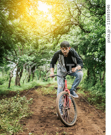 A guy riding a bike in the countryside, Person riding a bike in the countryside, Portrait of a guy in cap riding a bike on a country road, Bicyclist person on his bike on a country road forest. 118993546