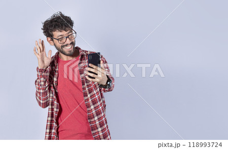 Smiling man making video call with his cellphone isolated, Positive teen guy making video call waving hands, Concept of smiling man saying hello by video call on cellphone Smiling man making video call with his cellphone isolated, Positive teen guy making video call waving hands, Concept of smiling man saying hello by video call on cellphone 118993724
