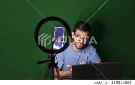 Guy with laptop making video blog on phone. Isolated person giving online classes. Man giving online classes with phone. Guy on a video call working from home. Online classes concept 118993891