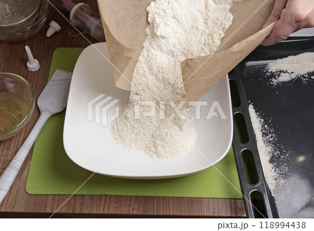 Process of making dough. Woman pour mixture of powdered sugar and almond flour into bowl in kitchen. Baking macarons at home. Hands close-up. Process of making dough. Woman pour mixture of powdered sugar and almond flour into bowl in kitchen. Baking macarons at home. Hands close-up. 118994438