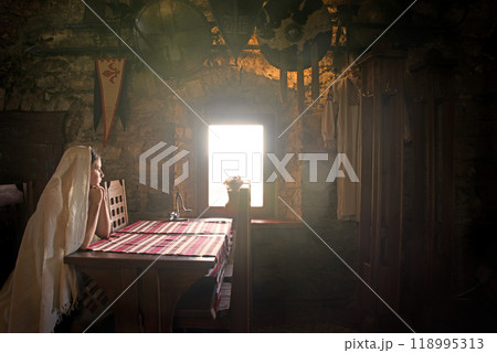 A girl sits at a table by the window in an ancient castle A girl sits at a table by the window in an ancient castle 118995313