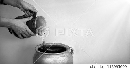 A hand holds a clay jar and pours water 118995699