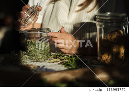 Woman opens a jar of dried mint. Work with herbs. Process  118995772