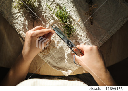 Top view of woman cuts twine to tie rosemary sprigs for drying. Herb preparation. Top view of woman cuts twine to tie rosemary sprigs for drying. Herb preparation. 118995784