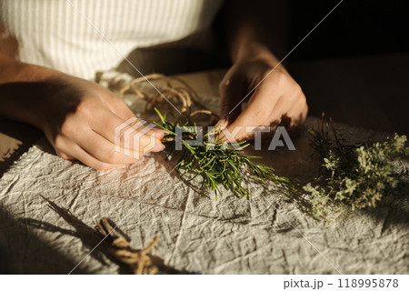 Woman uses natural twine to tie rosemary sprigs. Preparing fresh herbs for drying and spice use Woman uses natural twine to tie rosemary sprigs. Preparing fresh herbs for drying and spice use 118995878