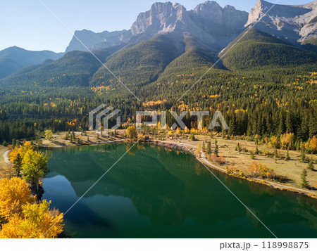 Aerial view of Canadian Rockies Autumn scenery in Quarry Lake, Canmore, Alberta, Canada. Yellow leaves forest, majestic mountains and blue sky reflected on the water. Aerial view of Canadian Rockies Autumn scenery in Quarry Lake, Canmore, Alberta, Canada. Yellow leaves forest, majestic mountains and blue sky reflected on the water. 118998875