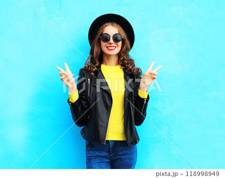 Fashion pretty smiling cool woman wearing a black rock style over colorful blue background 118998949