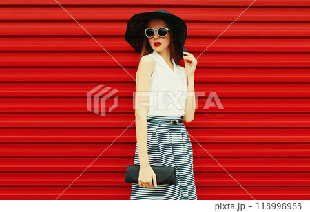 Portrait of stylish young woman model posing wearing summer round hat, handbag on red background 118998983