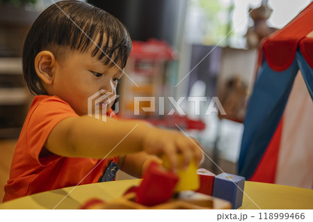 Little boy playing with multicolored geometric toy figures on a table. Colorful wooden children blocks. 118999466